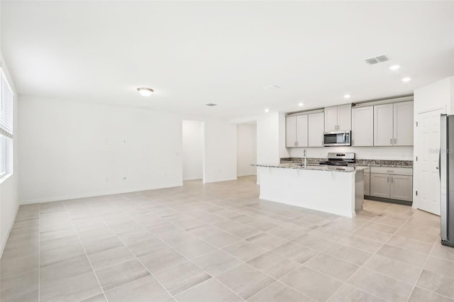 kitchen with appliances with stainless steel finishes, light stone counters, gray cabinetry, a kitchen island with sink, and light tile patterned floors