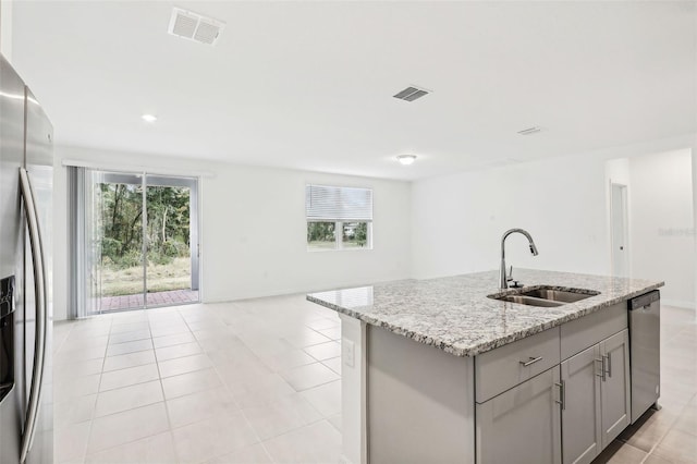 kitchen with gray cabinetry, light stone countertops, sink, an island with sink, and appliances with stainless steel finishes