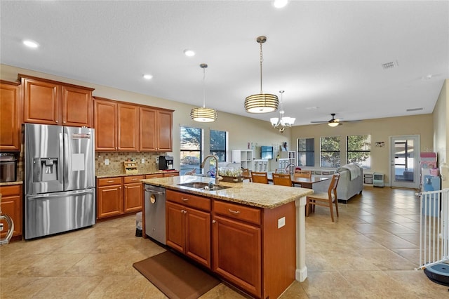 kitchen featuring light stone countertops, hanging light fixtures, a center island with sink, ceiling fan with notable chandelier, and appliances with stainless steel finishes