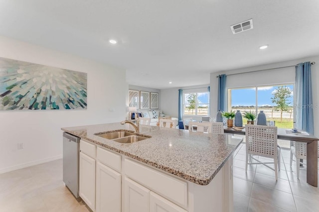 kitchen with light stone countertops, stainless steel dishwasher, sink, white cabinetry, and an island with sink