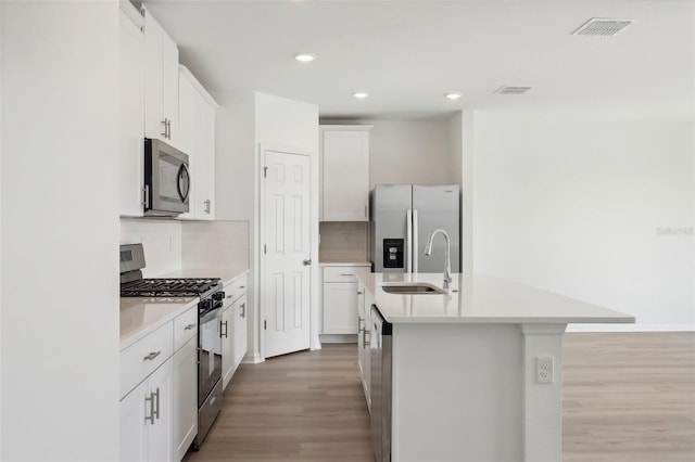 kitchen with white cabinetry, sink, stainless steel appliances, an island with sink, and light wood-type flooring