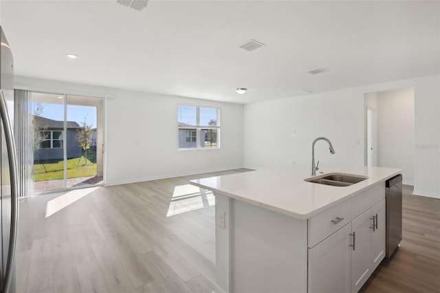 kitchen featuring white cabinets, sink, stainless steel dishwasher, an island with sink, and light hardwood / wood-style floors