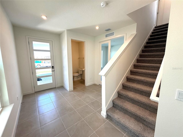 stairs with tile patterned floors, visible vents, baseboards, and a textured ceiling