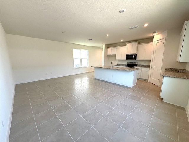 kitchen with an island with sink, white cabinets, light tile patterned flooring, and appliances with stainless steel finishes