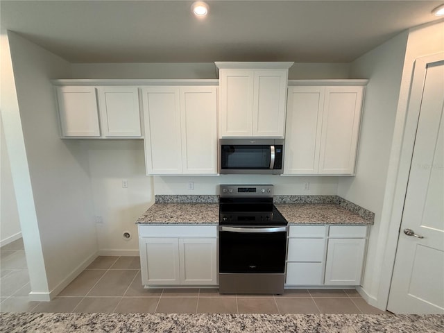 kitchen featuring light tile patterned floors, appliances with stainless steel finishes, white cabinetry, and baseboards