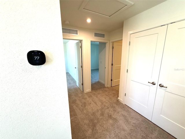 hallway with attic access, baseboards, visible vents, and carpet floors