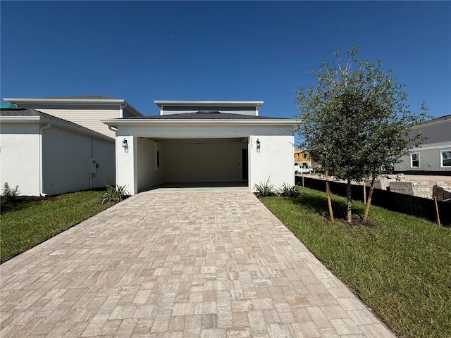 contemporary house with a front yard, fence, stucco siding, a garage, and decorative driveway