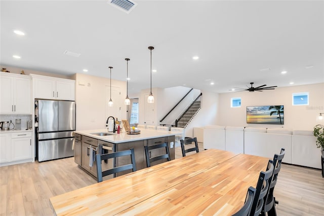 kitchen with stainless steel refrigerator, a center island with sink, white cabinets, and pendant lighting