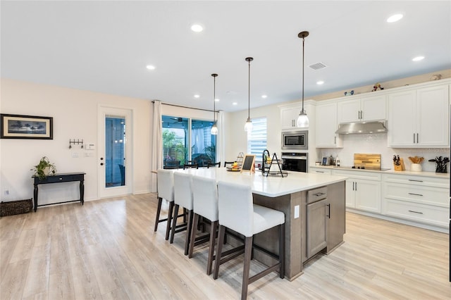 kitchen featuring hanging light fixtures, appliances with stainless steel finishes, white cabinetry, and a kitchen island with sink