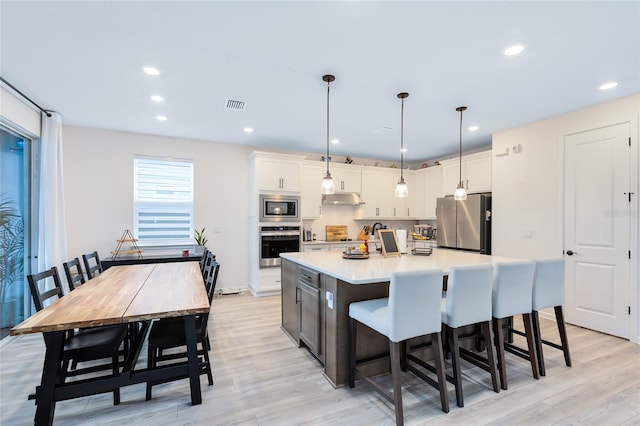 kitchen featuring light hardwood / wood-style flooring, decorative light fixtures, a center island with sink, white cabinets, and appliances with stainless steel finishes