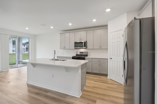 kitchen featuring sink, backsplash, light hardwood / wood-style floors, a center island with sink, and appliances with stainless steel finishes