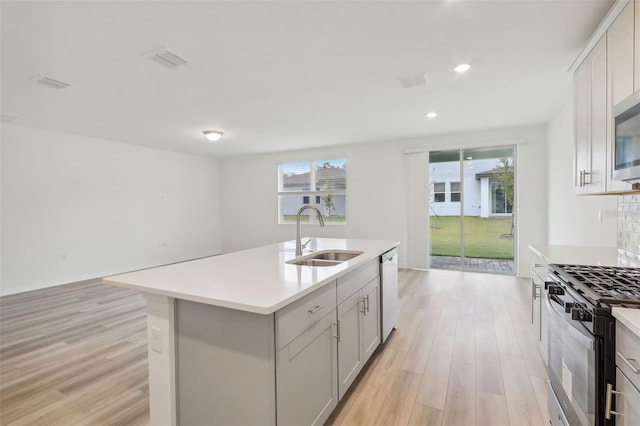 kitchen featuring a center island with sink, stainless steel gas range oven, a healthy amount of sunlight, and sink