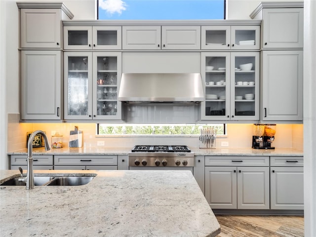 kitchen with sink, wall chimney exhaust hood, gray cabinets, light wood-type flooring, and light stone counters