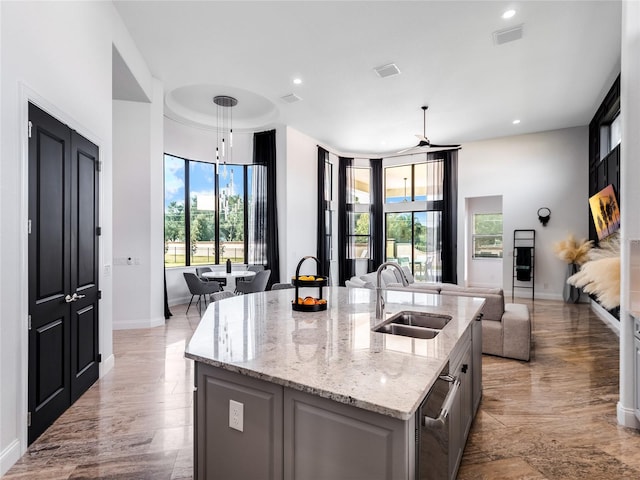 kitchen featuring a wealth of natural light, light stone counters, a kitchen island with sink, and sink