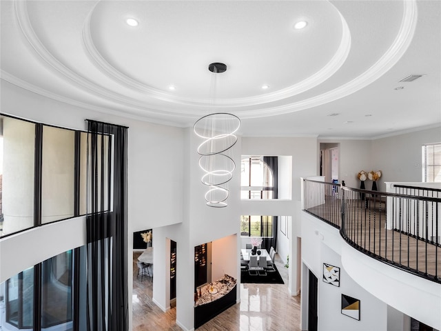 hallway with a tray ceiling, crown molding, a chandelier, and light wood-type flooring