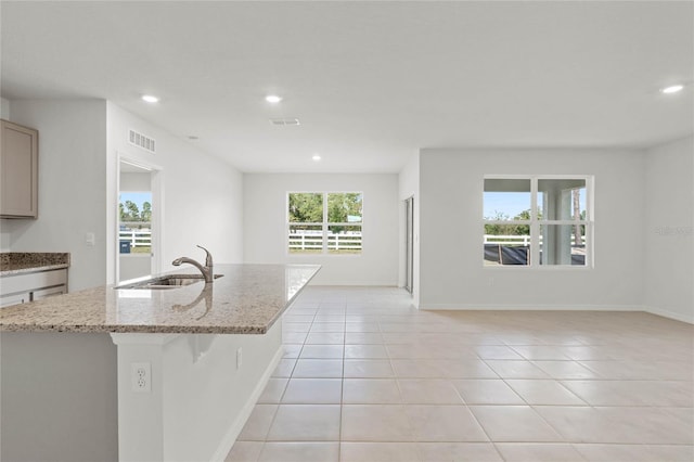 kitchen with sink, light stone counters, an island with sink, a breakfast bar area, and light tile patterned floors