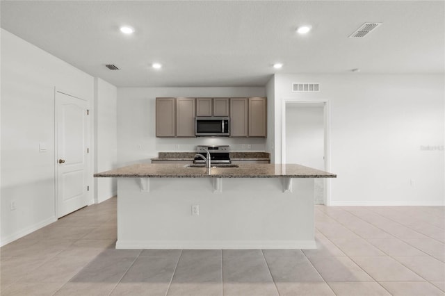 kitchen with sink, a kitchen island with sink, dark stone counters, a breakfast bar area, and stainless steel appliances