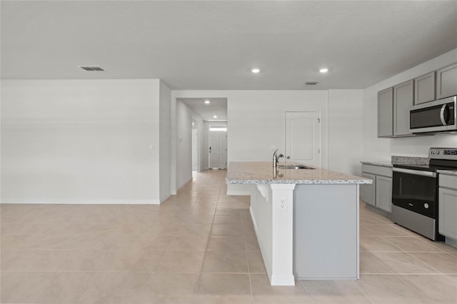 kitchen featuring a center island with sink, appliances with stainless steel finishes, gray cabinets, and light stone countertops