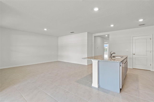 kitchen with light tile patterned flooring, sink, a kitchen island with sink, and light stone counters