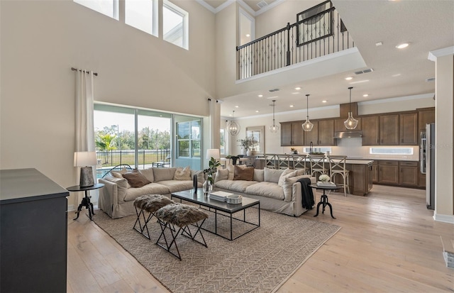 living room with crown molding, a towering ceiling, and light wood-type flooring