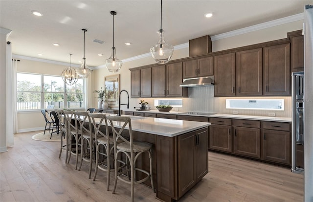 kitchen featuring a breakfast bar area, a kitchen island with sink, hanging light fixtures, and light wood-type flooring