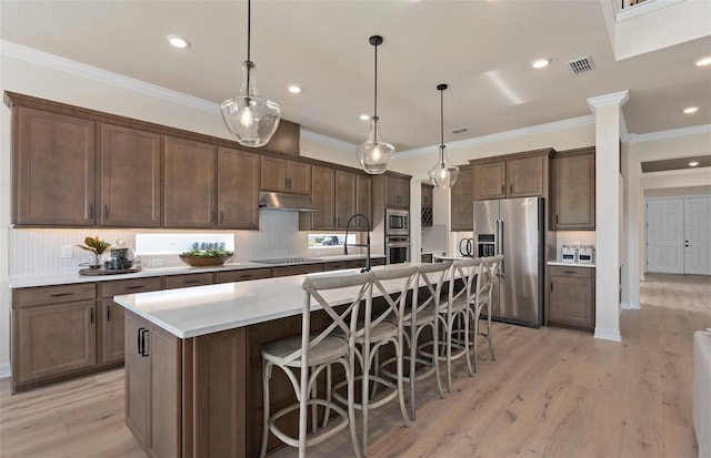 kitchen featuring a breakfast bar, stainless steel appliances, a kitchen island with sink, pendant lighting, and light hardwood / wood-style flooring