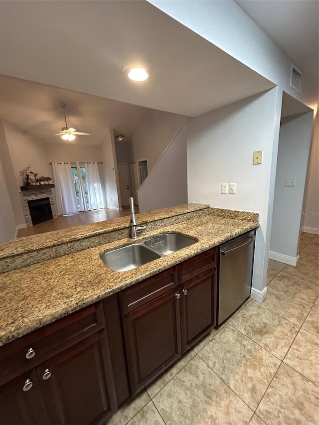 kitchen featuring dishwasher, a stone fireplace, sink, light stone countertops, and dark brown cabinets