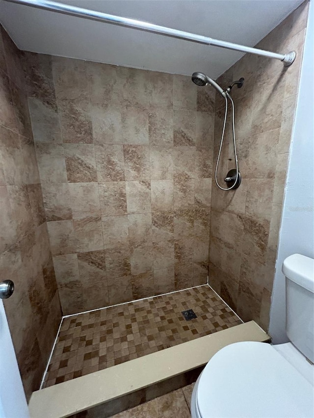 bathroom with a tile shower, toilet, and tile patterned floors