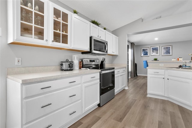 kitchen with stainless steel appliances, sink, white cabinets, light hardwood / wood-style floors, and lofted ceiling