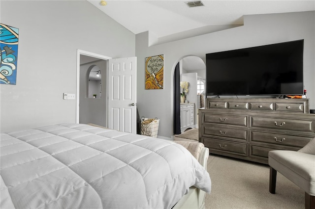 bedroom with ensuite bathroom, lofted ceiling, and light carpet