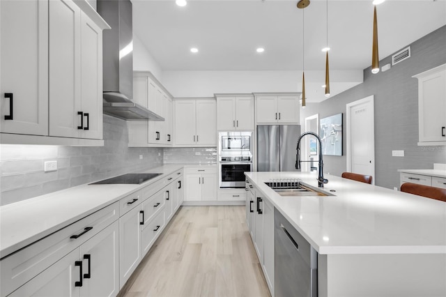 kitchen with a kitchen island with sink, sink, wall chimney exhaust hood, decorative light fixtures, and stainless steel appliances