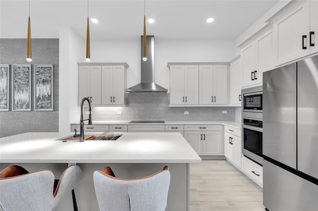 kitchen featuring wall chimney range hood, sink, decorative light fixtures, white cabinetry, and stainless steel appliances