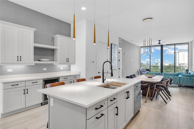 kitchen with white cabinetry, beverage cooler, an island with sink, light hardwood / wood-style floors, and pendant lighting