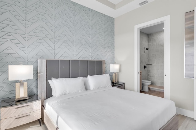 bedroom with ensuite bathroom, tile walls, and light hardwood / wood-style flooring