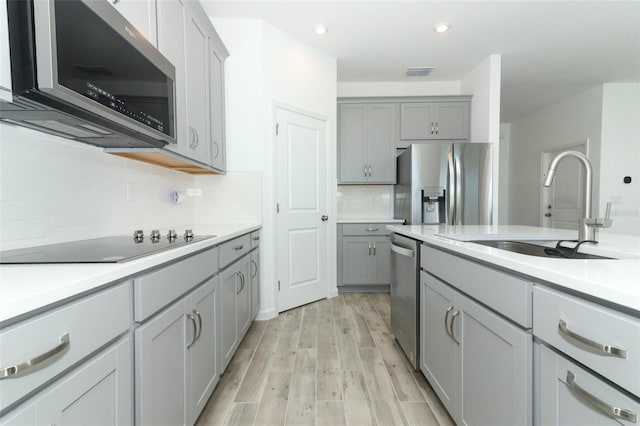 kitchen featuring appliances with stainless steel finishes, backsplash, gray cabinetry, sink, and light hardwood / wood-style flooring