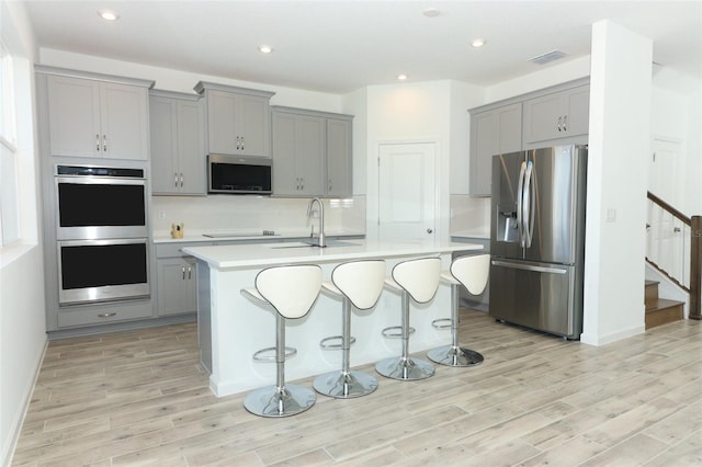 kitchen with a kitchen breakfast bar, gray cabinets, an island with sink, and appliances with stainless steel finishes