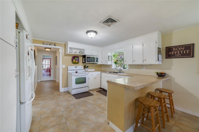 kitchen with kitchen peninsula, white appliances, white cabinetry, and a healthy amount of sunlight