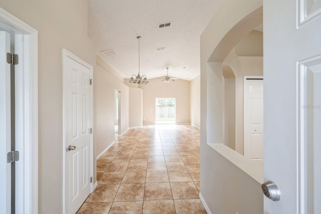 hallway featuring a textured ceiling, light tile patterned floors, vaulted ceiling, and an inviting chandelier