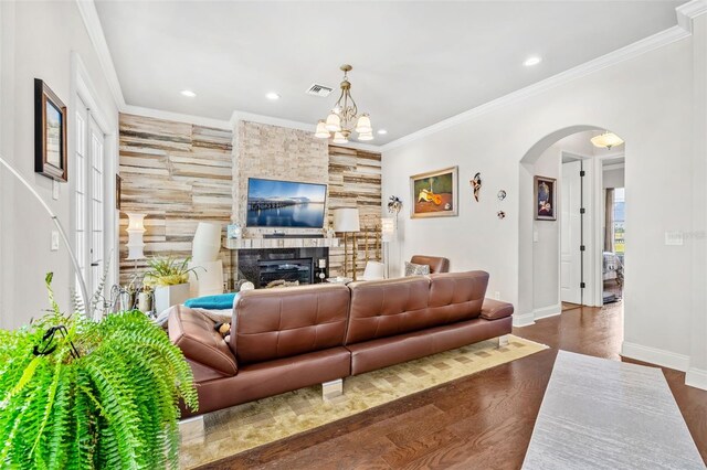 living room featuring dark hardwood / wood-style floors, a stone fireplace, ornamental molding, and an inviting chandelier