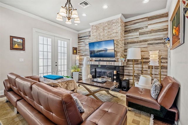 living room with french doors, a stone fireplace, ornamental molding, a notable chandelier, and wood-type flooring