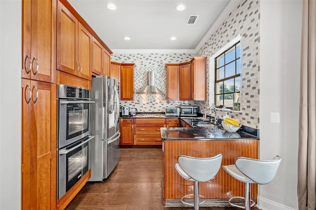 kitchen with appliances with stainless steel finishes, wall chimney exhaust hood, crown molding, sink, and dark hardwood / wood-style floors