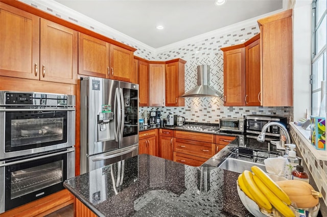 kitchen featuring crown molding, wall chimney exhaust hood, dark stone countertops, appliances with stainless steel finishes, and tasteful backsplash