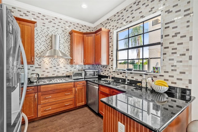 kitchen featuring backsplash, stainless steel appliances, crown molding, wall chimney range hood, and dark stone countertops