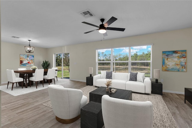 living room featuring a healthy amount of sunlight, ceiling fan with notable chandelier, and light wood-type flooring