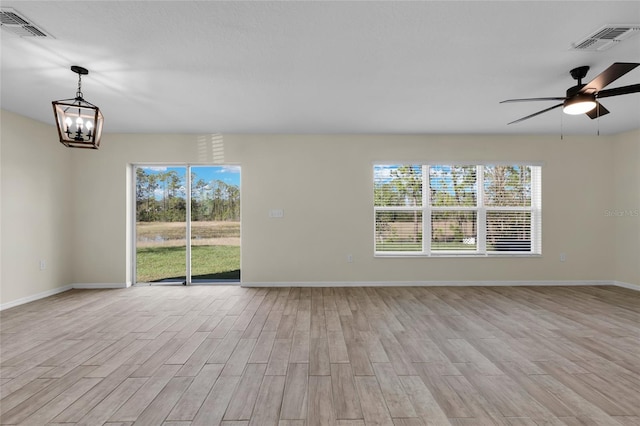 spare room with ceiling fan with notable chandelier and light wood-type flooring