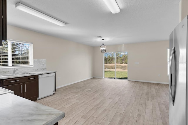 kitchen featuring stainless steel fridge, white dishwasher, dark brown cabinetry, tasteful backsplash, and decorative light fixtures