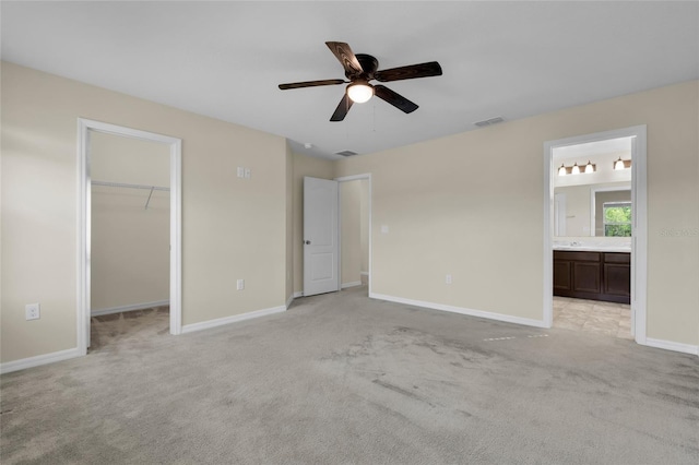 unfurnished bedroom featuring ceiling fan, ensuite bathroom, a walk in closet, light colored carpet, and a closet