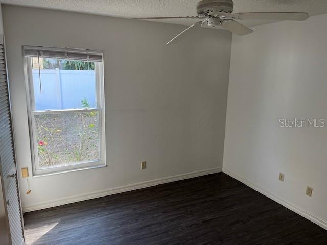 empty room with a textured ceiling, ceiling fan, and dark wood-type flooring