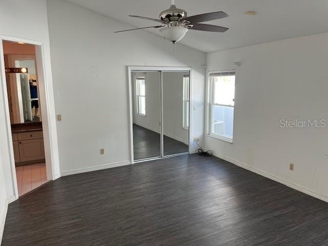 unfurnished bedroom featuring lofted ceiling, dark wood-type flooring, ensuite bath, ceiling fan, and a closet