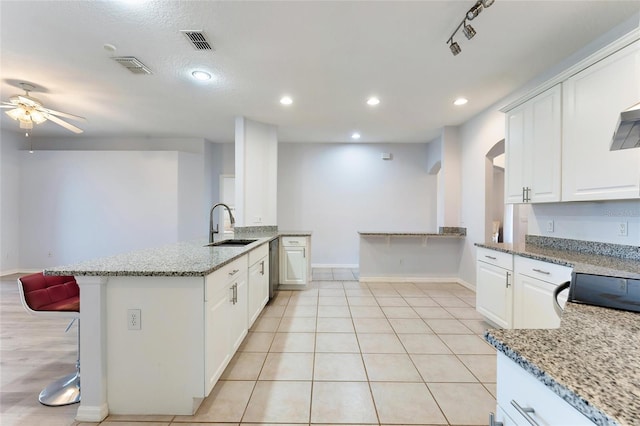 kitchen with white cabinets, light stone countertops, sink, and a breakfast bar area